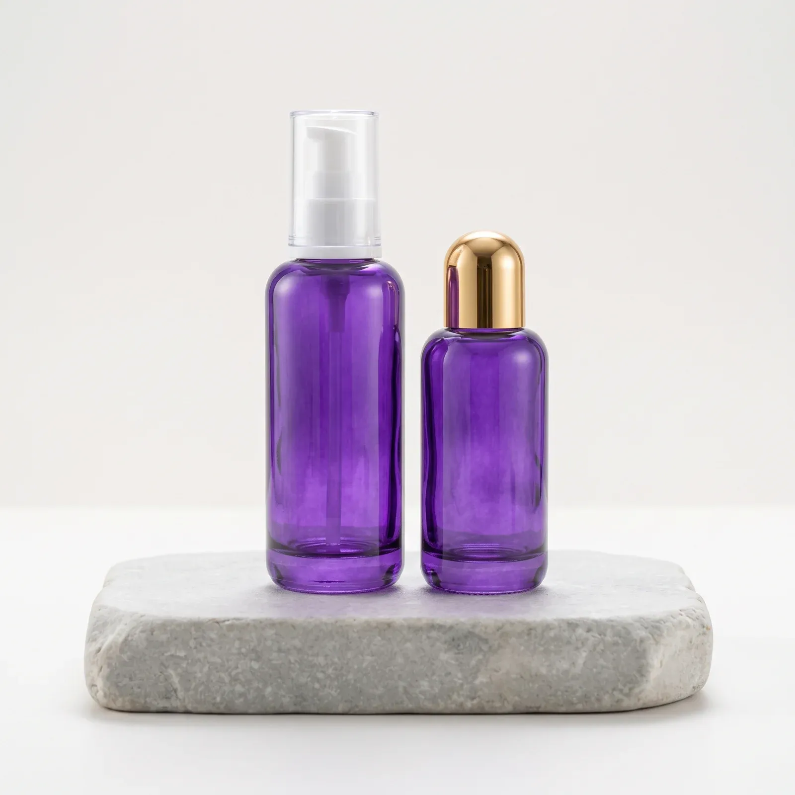 Violet glass bottle with white lotion pump beside a gold-domed violet bottle on a stone pedestal