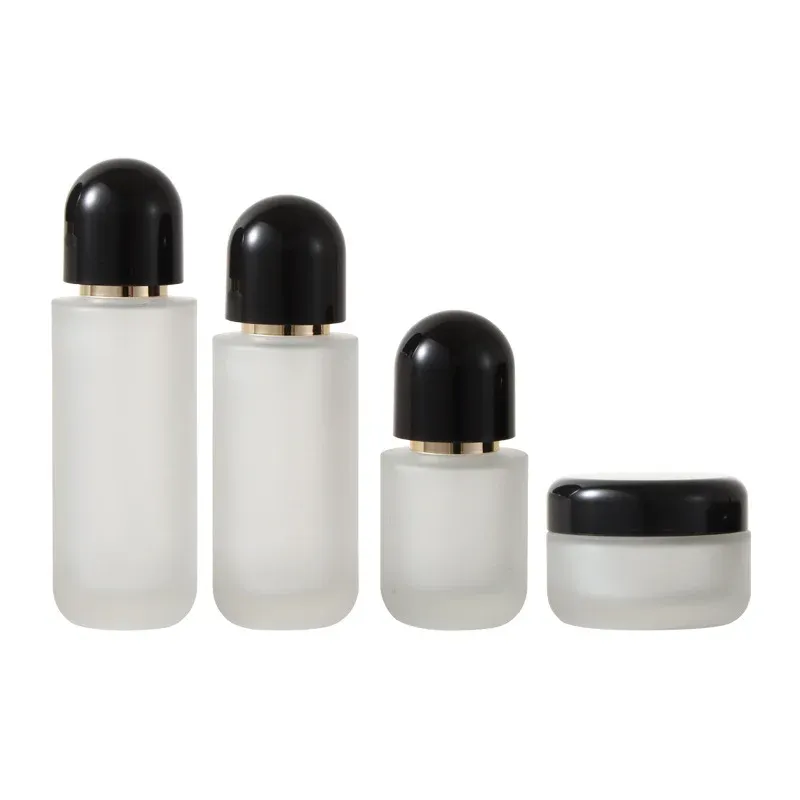 Four-piece frosted glass set with black dome caps: three bottles and a cream jar on white background