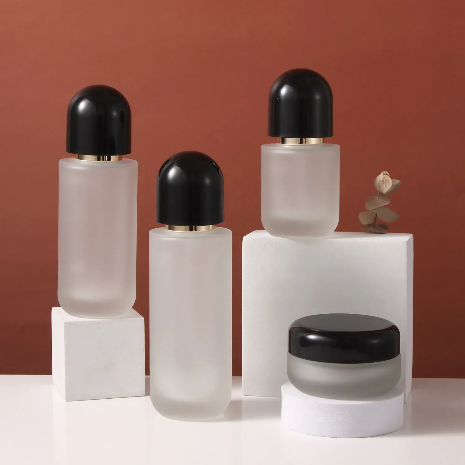 Frosted glass skincare set with black dome caps: three pump bottles and a cream jar on white blocks