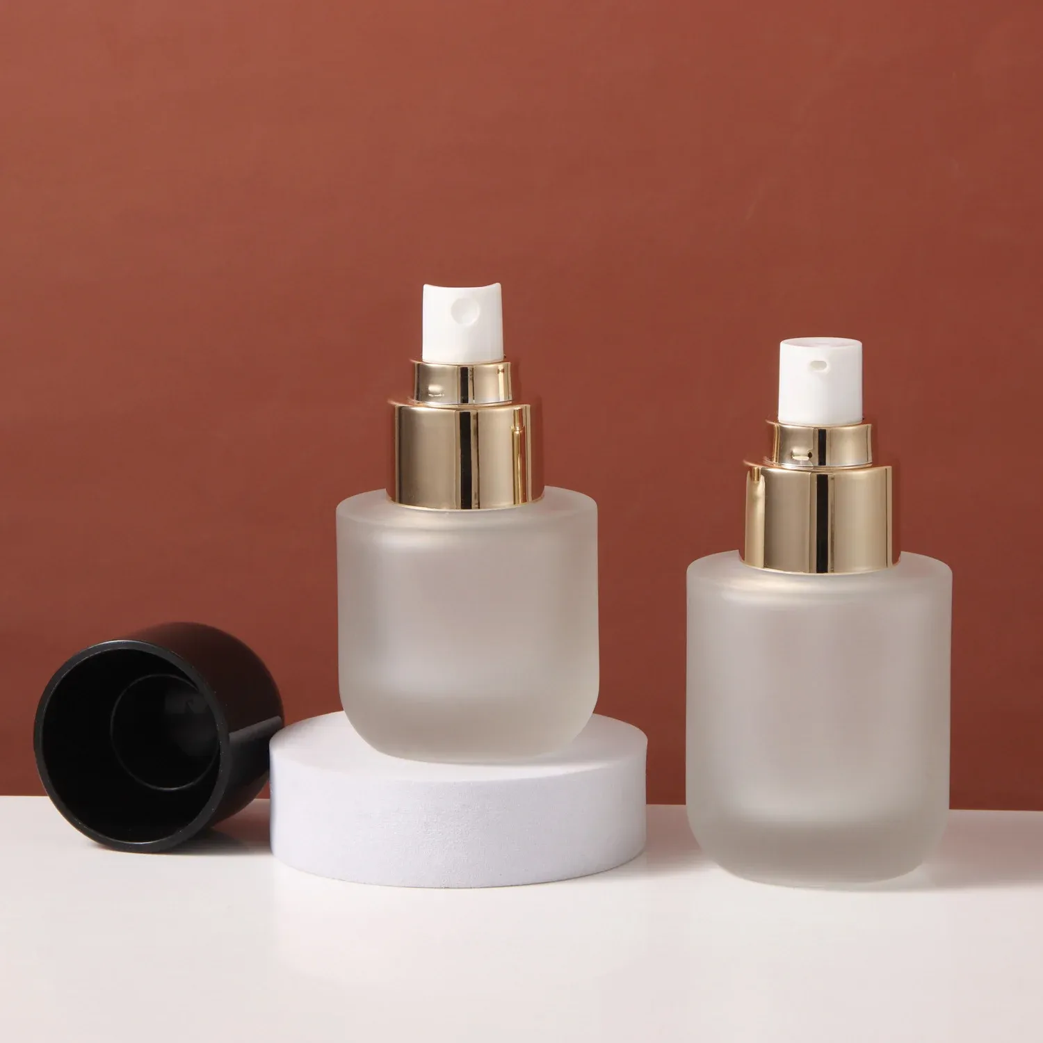 Two frosted glass bottles with gold lotion pumps, black dome cap removed beside them
