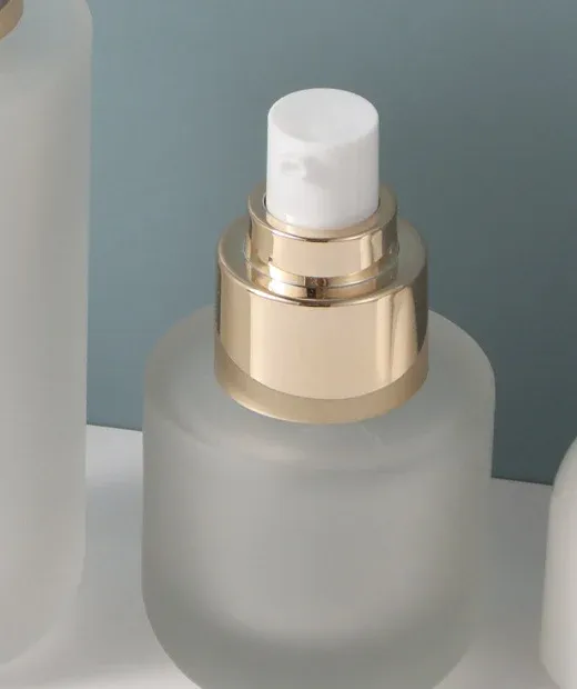 Close-up of gold pump collar and white actuator on a small frosted glass bottle