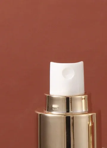 Close-up of the gold fine-mist sprayer with white actuator on a frosted glass bottle