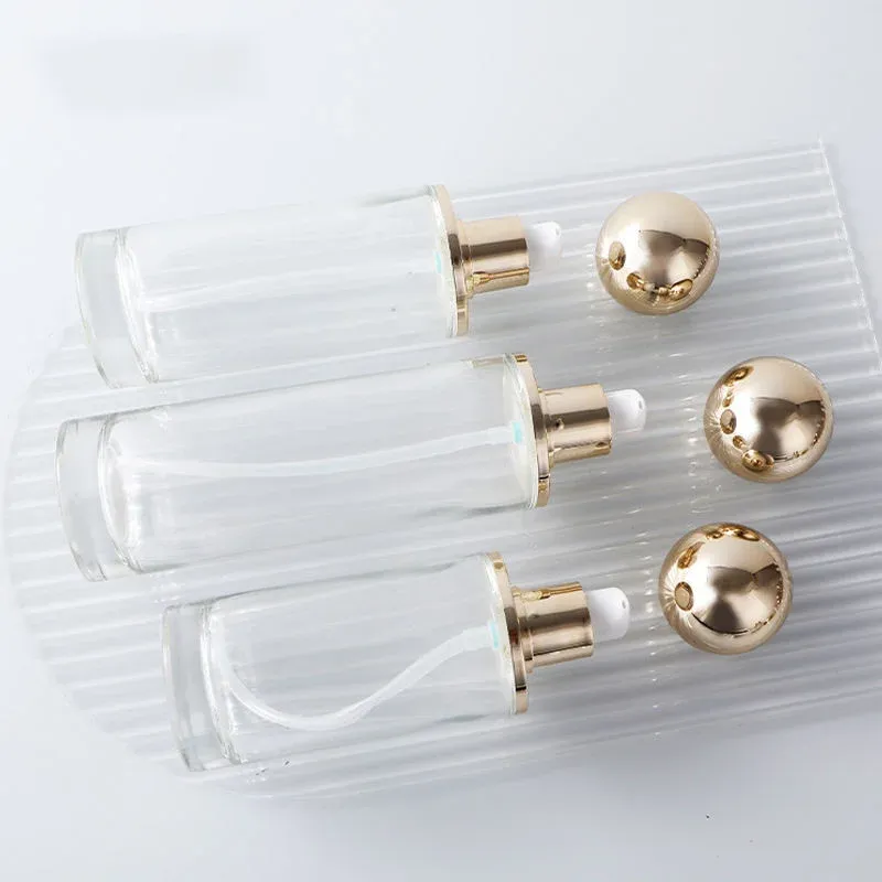 Three clear glass bottles with gold ball lids lying on a ribbed glass tray