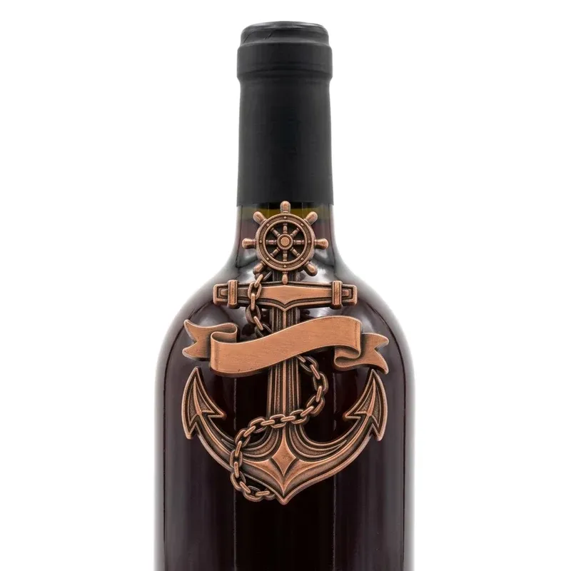 Antique copper anchor challenge coin mounted on dark red wine bottle shoulder below the black capsule