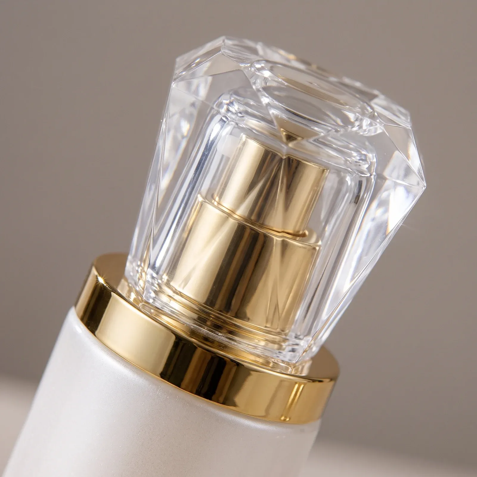 Macro detail of a faceted crystal-clear cap over the gold pump collar of a pearl-white glass bottle