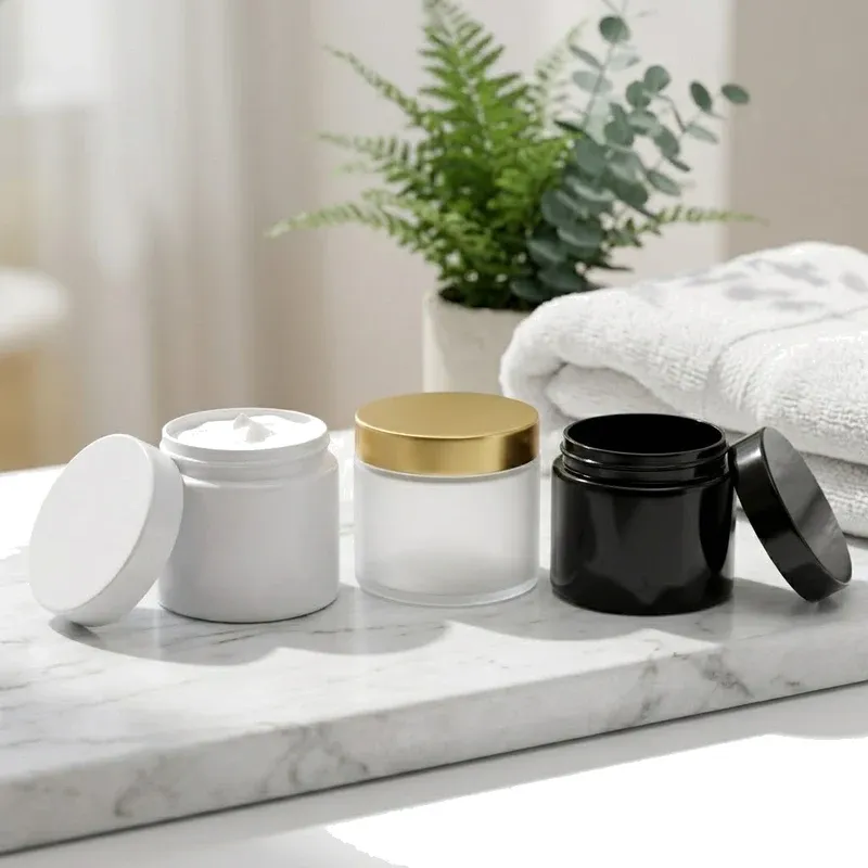 Three mask jars on a marble vanity in a bright spa scene: white jar open with cream, frosted gold-lid jar, black jar