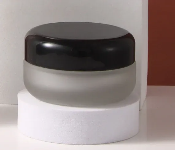 Frosted glass cream jar with glossy black dome lid on a white pedestal