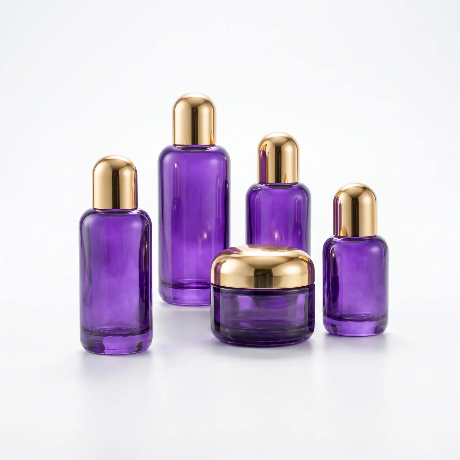 Five-piece violet glass set lineup on white background: four bottles tall to small with gold dome caps and one cream jar