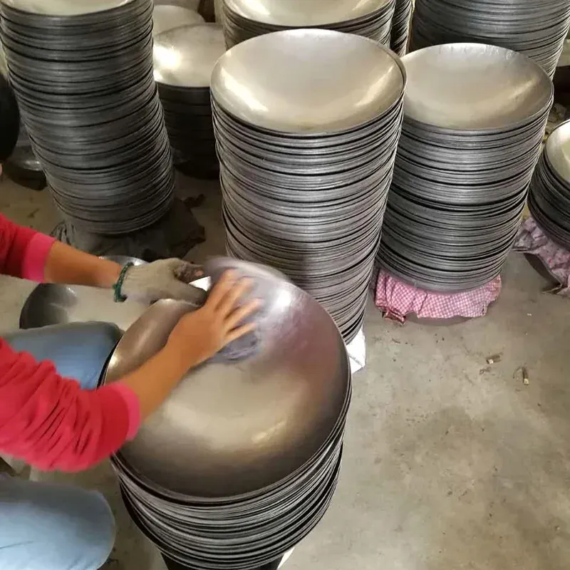 An operator working on the surface of a formed wok body beside stacked cookware